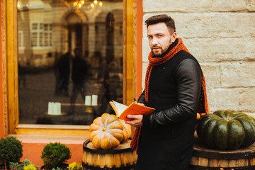 handsome and young man in a black coat reading a book outdoors
