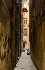 View into a gritty narrow street leading to a backyard between the buildings in the ancient part of the city of Genoa, Italy.