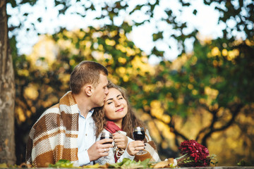 Loving couple with wine glasses embracing at the autumn park.