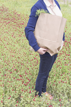 Woman carrying groceries through af field of flowers.