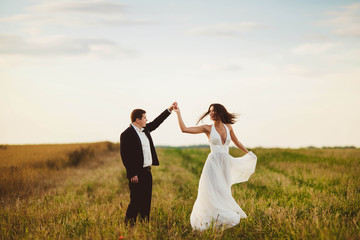 happy and young bride and groom dancing in the field