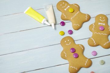 Hand decorated gingerbread men on a painted wooden table background, with candy, icing tubes and empty space at side