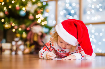 Little girl in red christmas hat writes letter to Santa Claus