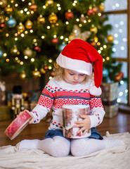 Young girl in red santa hat opening Christmas gifts