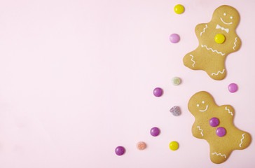 Hand decorated gingerbread men on a pastel pink background, with sweets and blank space at side