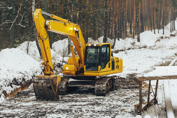 heavy yellow excavator with shovel standing among snowy forest