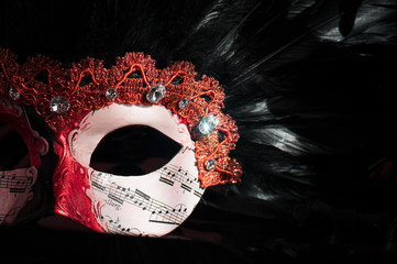venezianische Gesichtsmaske in rot und weiß mit schwarzen Federn vor dunklem Hintergrund