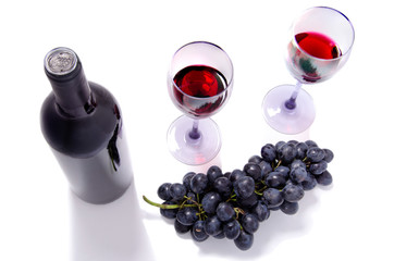 bottle of red wine,  wine glasses and grapes on white table