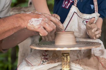 Hands of two people create pot on potter's wheel. Teaching ukrainian traditional crafts. Focus on the hands