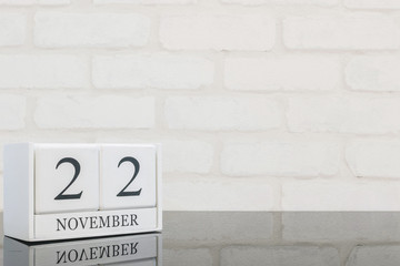 Closeup white wooden calendar with black 22 november word on black glass table and white brick wall textured background with copy space , selective focus at the calendar