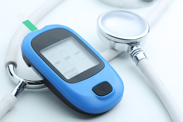 Blood glucose meter and stethoscope on white background