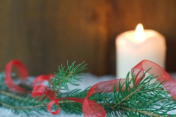 Branch of Christmas tree with red ribbon and a burning candle in snow