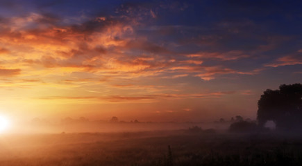 Naklejka na ściany i meble majestic dramatic scene. fantastic foggy sunset over the meadow with colorful clouds on the sky. picturesque rural landscape, misty morning. color in nature. soft selective focus