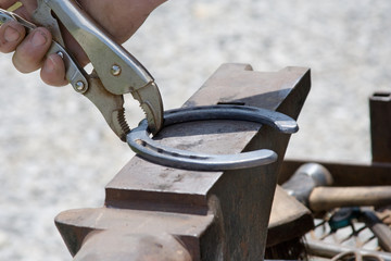 Shaping a Horseshoe on Anvil – A farrier or blacksmith is holding a hot horseshoe with pliers as he shapes it on an anvil.