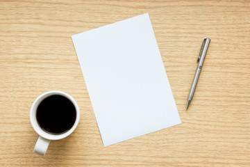 Workplace of wooden desk with a pen and empty white paper with a cup of coffee