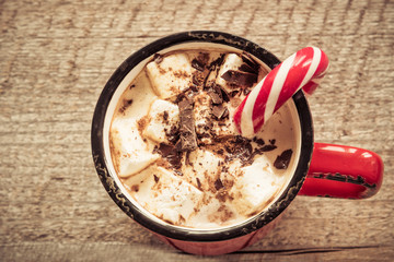 Christmas drink. Hot chocolate with marshmallows and candy cane on the wooden background. Hot cocoa with marshmallows. New Year. Holiday card. Rustic style. Close up. Toned image.