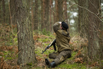 a military man in the woods with a Kalashnikov assault rifle, autumn forest with no leaves, green form, No face.