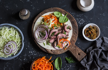 Steak tortilla with pickled carrots and cabbage on a wooden cutting board on dark background, top view