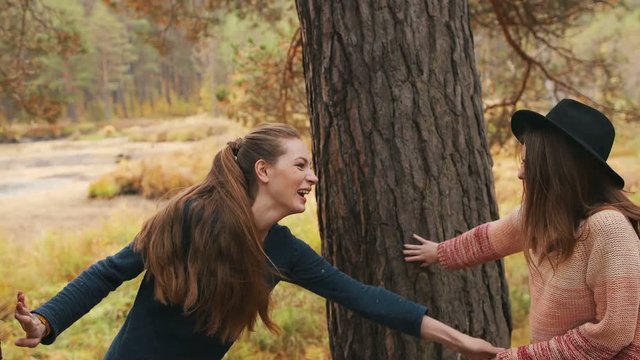Girls play tag in the autumn forest. One girl in nice hat. Girls have fun and laughing 