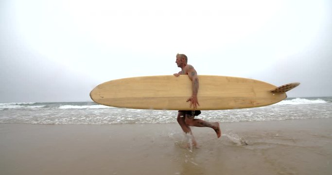 Mature Surfer Running Through the Ocean with Surfboard.