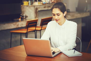 Young Caucasian woman working with laptop in coffee shop while listening with headphone