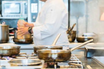 Chef heating saucepan on stove with coworker in background
