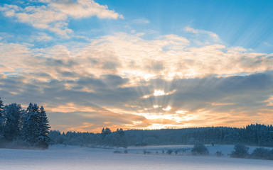 Frosty early morning winter panoramic scenery with rising sun sunbeam over frozen snowfield and...