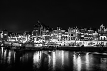 Obraz premium AMSTERDAM, NETHERLANDS - DECEMBER 14, 2015: Black-white photo of cruise boat moving on night canals of Amsterdam in Amsterdam, Netherlands.