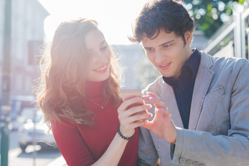Young beautiful couple in love using smart phone together outdoor in the city - interaction, love, technology concept