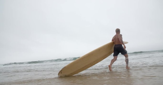 Mature Surfer Runs into the Ocean Waves.