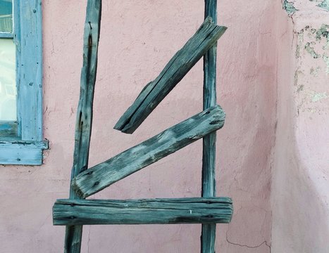 Ausschnitt einer Hauswand mit blassblauem Fensterrahmen und zerbrochener Holzleiter