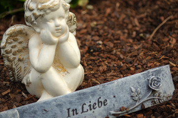 little angel sculpture decorate in small garden with flowers in front it and a sign - in love - in German