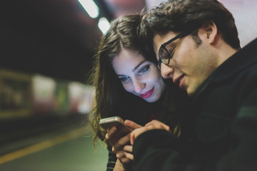 Young beautiful couple in love using smart phone together in the subway - interaction, love,...