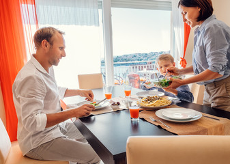 Mother brings a dish of meal at table to her hungry family