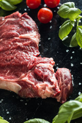 Fresh steak served with spices, tomatoes and leafs of basil on marble background. Uncooked beefsteak cooking on a kitchen. Delicious, spicy, juicy meat with copy space closeup.