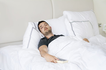 Handsome young man happily sleeping in white bed with book in the hand