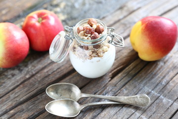 Naklejka na ściany i meble Glass jar with yogurt, granolla and almond nuts in it. Nectarin and apples are on the wooden backgound with spoons closed to the jar.