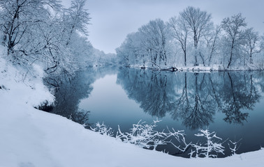 Winter forest on the river at sunset. Colorful landscape with snowy trees, beautiful frozen river...