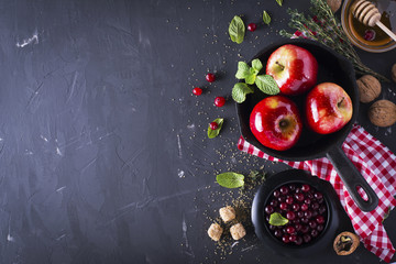 Juicy red fragrant apples for baking a dessert with cranberries, honey, nuts, mint, thyme and sugar cane   black iron skillet on  dark background