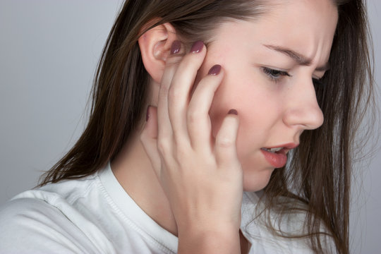 Young woman has a sore ear.  girl suffering from otitis, closeup   over gray background