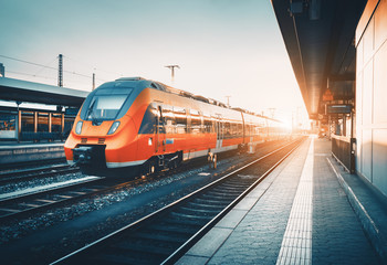Modern high speed red commuter train at the railway station at colorful sunset. Railroad with...