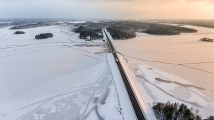 Aerial view at the highway with semitrucks driving on the bridge across frozen river. Winter road is in north at polar night, Russia
