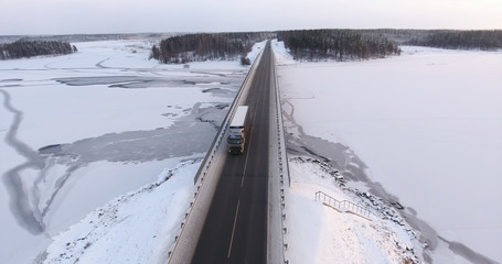 Semitruck driving on winter country road on the bridge across frozen river. Russia. Aerial view