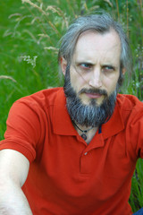 bearded angry man sitting in a green background on sunny day, potrait