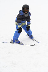 Fototapeta na wymiar Child boy skiing in mountains. Active teenager kid with safety helmet and goggles. Ski race for young children. Winter sport for family. Kids ski lesson in alpine school. Young skier racing in snow