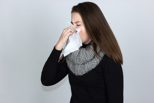 Portrait of a pretty woman in turtleneck sweaterand and scarf  having flu. girl blowing nose standing over gray background and black and white with red accent