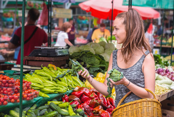 Young woman buying vegetables and fruits at local food market.