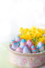 Basket of Hand Painted Easter Eggs with Daffodils on Table Vertical with Copy Space & Bokeh