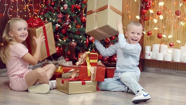 Boy and girl playing with gifts under the Christmas tree.