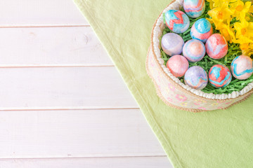 Basket of Hand Painted Easter Eggs with Daffodils on Table From Above with Copy Space